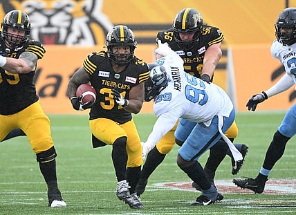 Sep 5, 2022; Hamilton, Ontario, CAN;   Hamilton Tiger-Cats running back Sean Thomas Erlington (31) carries the ball past Toronto Argonauts lineman Dewayne Hendrix (99) in the first half of the annual Labor Day Classic at Tim Hortons Field. Mandatory Credit: Dan Hamilton-USA TODAY Sports