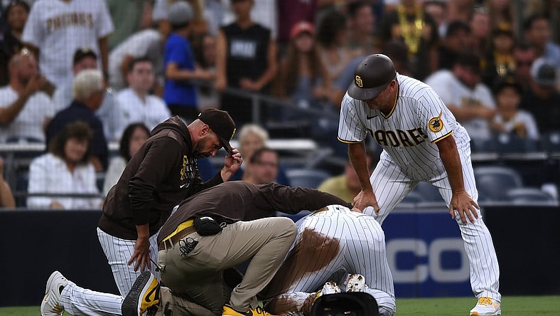 Jul 30, 2021; San Diego, California, USA; San Diego Padres shortstop Fernando Tatis Jr. (second from right) is looked at by a trainer after an injury during the first inning against the Colorado Rockies as Padres manager Jayce Tingler (left) and third base coach Bobby Dickerson (right) look on at Petco Park. Mandatory Credit: Orlando Ramirez-USA TODAY Sports