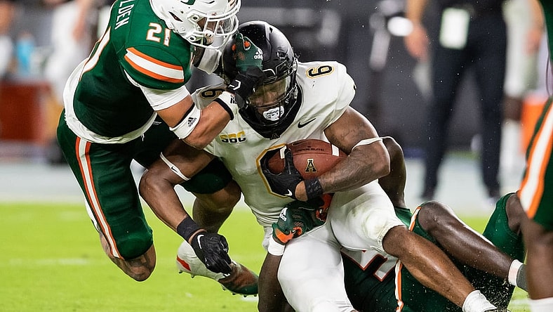 Sep 11, 2021; Miami Gardens, Florida, USA; Appalachian State Mountaineers running back Camerun Peoples (6) is tackled by Miami Hurricanes safety Bubba Bolden (21) and safety Amari Carter (5) during the second quarter at Hard Rock Stadium. Mandatory Credit: Richard Graulich-USA TODAY Sports