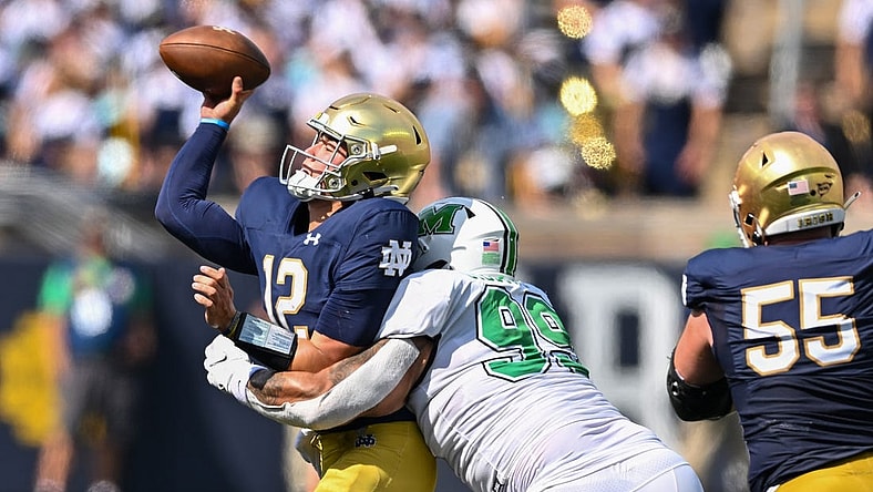 Sep 10, 2022; South Bend, Indiana, USA; Notre Dame Fighting Irish quarterback Tyler Buchner (12) throws as he is hit by Marshall Thundering Herd defensive lineman Isaiah Gibson, Sr. (99) in the first quarter at Notre Dame Stadium. Mandatory Credit: Matt Cashore-USA TODAY Sports