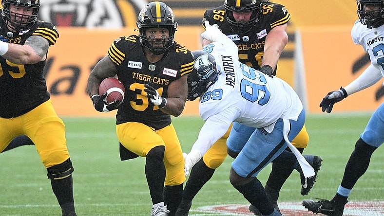 Sep 5, 2022; Hamilton, Ontario, CAN; Hamilton Tiger-Cats running back Sean Thomas Erlington (31) carries the ball past Toronto Argonauts lineman Dewayne Hendrix (99) in the first half of the annual Labor Day Classic at Tim Hortons Field. Mandatory Credit: Dan Hamilton-USA TODAY Sports