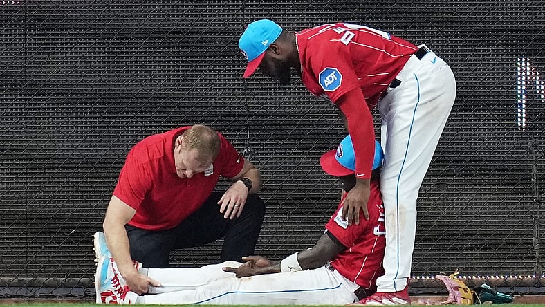 May 13, 2023; Miami, Florida, USA; Miami Marlins left fielder Bryan De La Cruz (14) holds up center fielder Jazz Chisholm Jr. (2) as he has his leg examined after colliding with the centerfield wall in the eighth inning against the Cincinnati Reds at loanDepot Park. Mandatory Credit: Jim Rassol-USA TODAY Sports