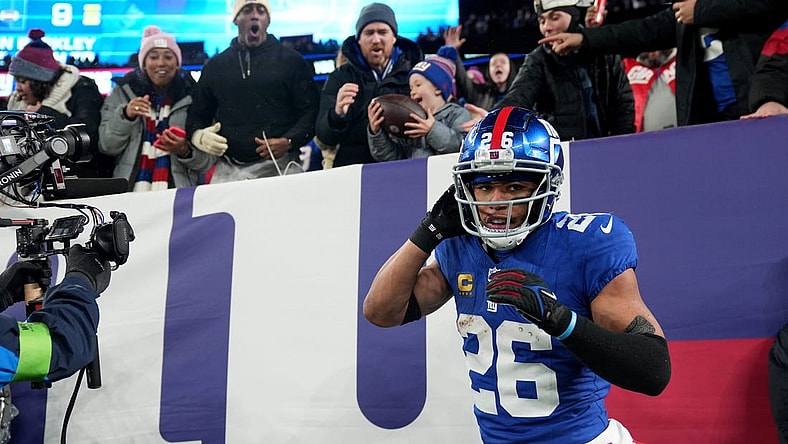 New York Giants running back Saquon Barkley (26) is shown after scoring a touchdown and giving the ball to Harrison Isaacs (background), 6. Harrison traveled with his father Christoper Isaacs (background) to attend his first NFL game, Sunday, January 7, 2024.
