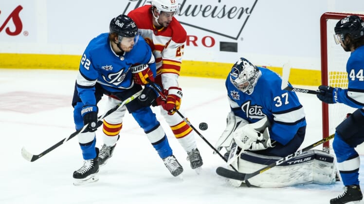 Feb 1, 2021; Winnipeg, Manitoba, CAN;  Winnipeg Jets goalie Connor Hellebuyck (37) makes a save with Calgary Flames forward Sean Monahan (23) looking for a rebound during the first period at Bell MTS Place. Mandatory Credit: Terrence Lee-USA TODAY Sports