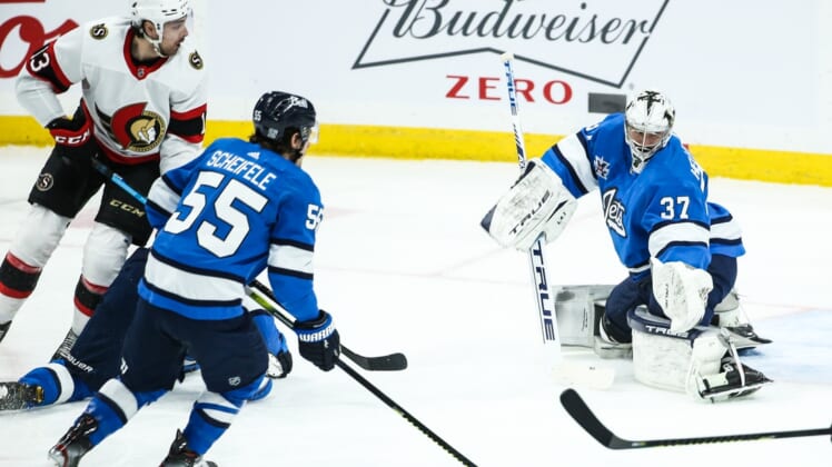 Feb 13, 2021; Winnipeg, Manitoba, CAN;  Winnipeg Jets goalie Connor Hellebuyck (37) makes a pad save with Ottawa Senators forward Nick Paul (13) and Winnipeg Jets forward Mark Scheifele (55) looking for a rebound during the first period at Bell MTS Place. Mandatory Credit: Terrence Lee-USA TODAY Sports