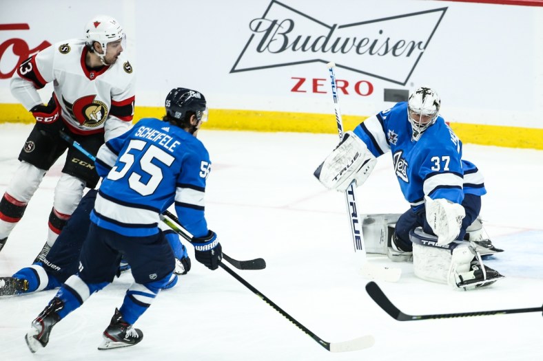 Feb 13, 2021; Winnipeg, Manitoba, CAN;  Winnipeg Jets goalie Connor Hellebuyck (37) makes a pad save with Ottawa Senators forward Nick Paul (13) and Winnipeg Jets forward Mark Scheifele (55) looking for a rebound during the first period at Bell MTS Place. Mandatory Credit: Terrence Lee-USA TODAY Sports