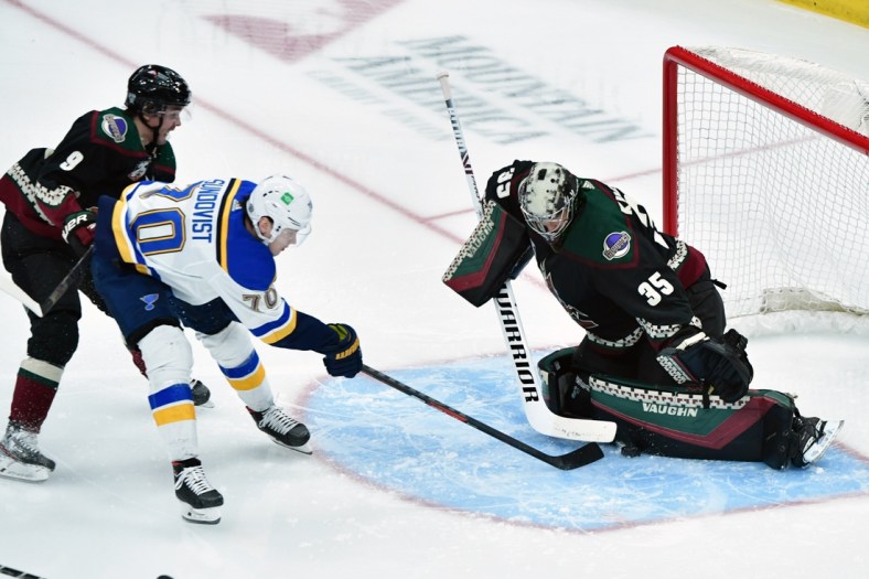 Feb 15, 2021; Glendale, Arizona, USA;  
St. Louis Blues center Oskar Sundqvist (70) reaches for the puck as Arizona Coyotes right wing Clayton Keller (9) and goaltender Darcy Kuemper (35) defend during the second period at Gila River Arena. Mandatory Credit: Matt Kartozian-USA TODAY Sports