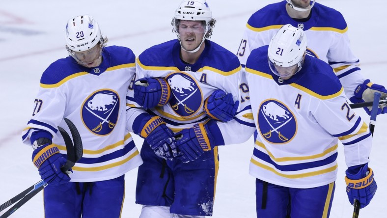 Feb 20, 2021; Newark, New Jersey, USA; Buffalo Sabres defenseman Jake McCabe (19) reacts while being helped off the ice by teammates after suffering an apparent injury during the during the third period against the New Jersey Devils at Prudential Center. Mandatory Credit: Vincent Carchietta-USA TODAY Sports