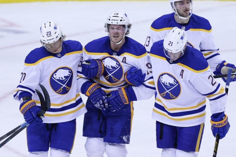 Feb 20, 2021; Newark, New Jersey, USA; Buffalo Sabres defenseman Jake McCabe (19) reacts while being helped off the ice by teammates after suffering an apparent injury during the during the third period against the New Jersey Devils at Prudential Center. Mandatory Credit: Vincent Carchietta-USA TODAY Sports