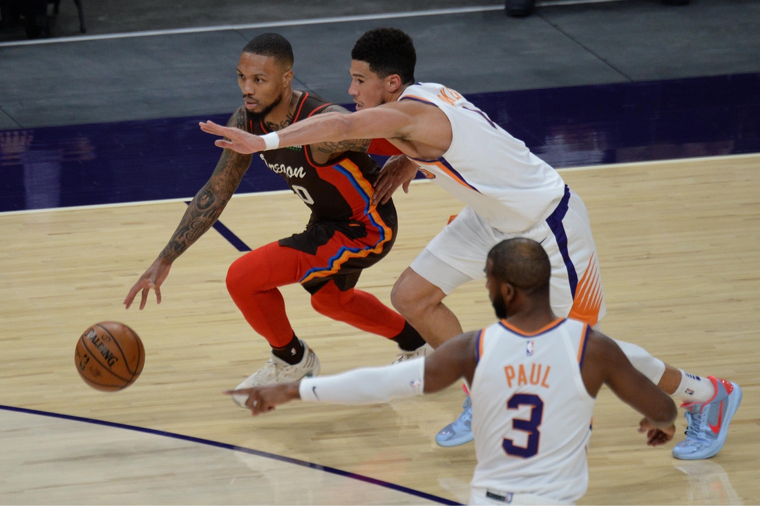 Feb 22, 2021; Phoenix, Arizona, USA; Portland Trail Blazers guard Damian Lillard (0) dribbles against Phoenix Suns guard Devin Booker (1) during the first half at Phoenix Suns Arena. Mandatory Credit: Joe Camporeale-USA TODAY Sports