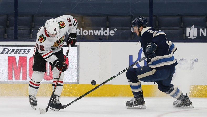 Feb 25, 2021; Columbus, Ohio, USA; Chicago Blackhawks right wing  Alex DeBrincat (12) and Columbus Blue Jackets defenseman Andrew Peeke (2) battle for control of the puck during the second period at Nationwide Arena. Mandatory Credit: Russell LaBounty-USA TODAY Sports