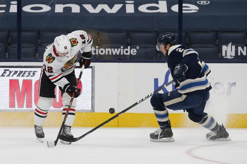 Feb 25, 2021; Columbus, Ohio, USA; Chicago Blackhawks right wing  Alex DeBrincat (12) and Columbus Blue Jackets defenseman Andrew Peeke (2) battle for control of the puck during the second period at Nationwide Arena. Mandatory Credit: Russell LaBounty-USA TODAY Sports