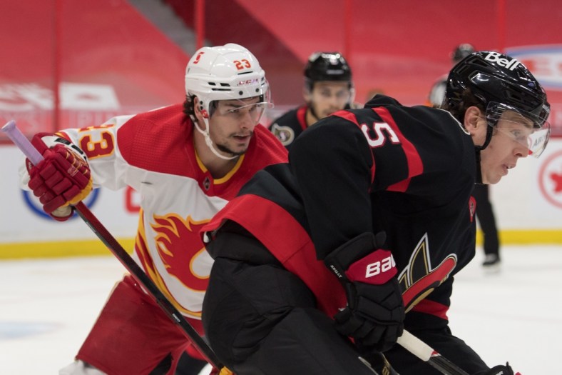 Feb 27, 2021; Ottawa, Ontario, CAN; Ottawa Senators defenseman Mike Reilly (5) chases the puck in front of Calgary Flames center Sean Monahan (23) in the first period at the Canadian Tire Centre. Mandatory Credit: Marc DesRosiers-USA TODAY Sports