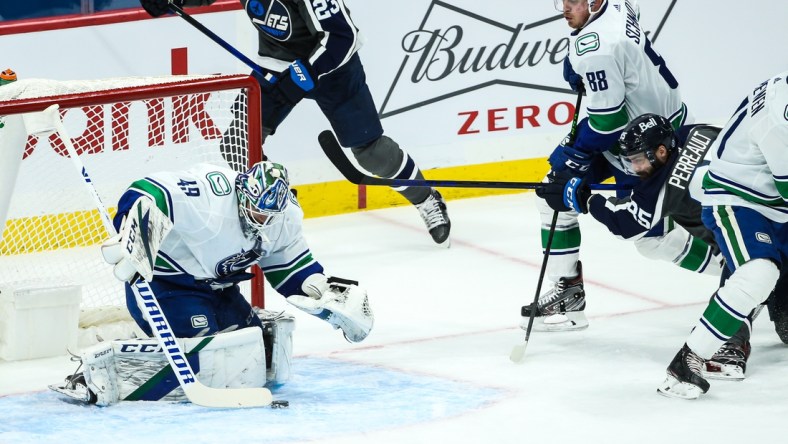 Mar 2, 2021; Winnipeg, Manitoba, CAN;  Vancouver Canucks goalie Braden Holtby (49) smothers the puck in front of Winnipeg Jets forward Matthieu Perreault (85) during the first period at Bell MTS Place. Mandatory Credit: Terrence Lee-USA TODAY Sports