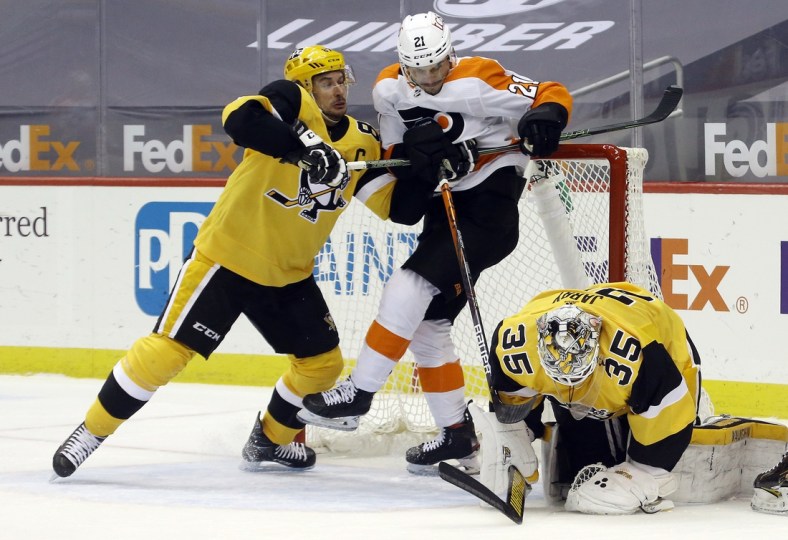 Mar 4, 2021; Pittsburgh, Pennsylvania, USA;  Pittsburgh Penguins center Sidney Crosby (87) defends Philadelphia Flyers left wing Scott Laughton (21) as Pittsburgh Penguins goaltender Tristan Jarry (35) covers the puck after a save during the second period at PPG Paints Arena. Mandatory Credit: Charles LeClaire-USA TODAY Sports