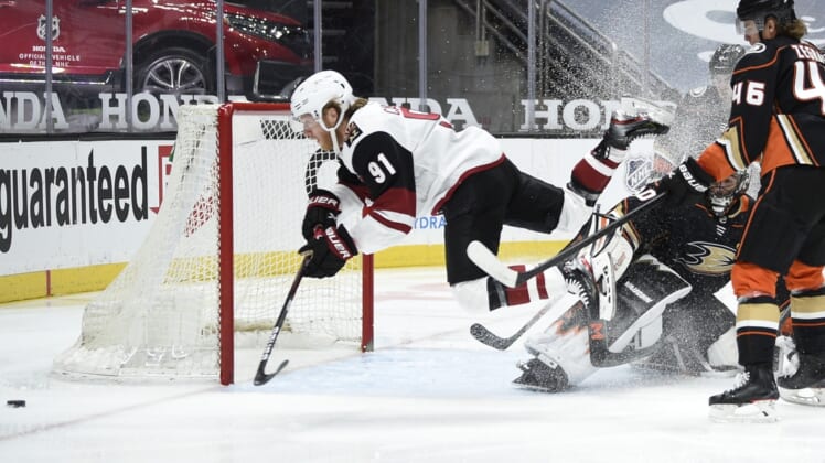 Mar 20, 2021; Anaheim, California, USA; Arizona Coyotes center Drake Caggiula (91) trips over Anaheim Ducks goalie Ryan Miller (30) while chasing the puck during the first period at Honda Center. Mandatory Credit: Kelvin Kuo-USA TODAY Sports