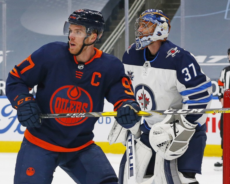 Mar 20, 2021; Edmonton, Alberta, CAN; Edmonton Oilers forward Connor McDavid (97) looks for a puck in front of Winnipeg Jets goaltender Connor Hellebuyck (37) during the first period at Rogers Place. Mandatory Credit: Perry Nelson-USA TODAY Sports