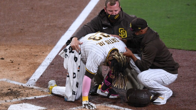 Apr 5, 2021; San Diego, California, USA; San Diego Padres shortstop Fernando Tatis Jr. (23) is looked at by a trainer after injuring himself during a swing as manager Jayce Tingler (R) assists during the third inning against the San Francisco Giants at Petco Park. Mandatory Credit: Orlando Ramirez-USA TODAY Sports