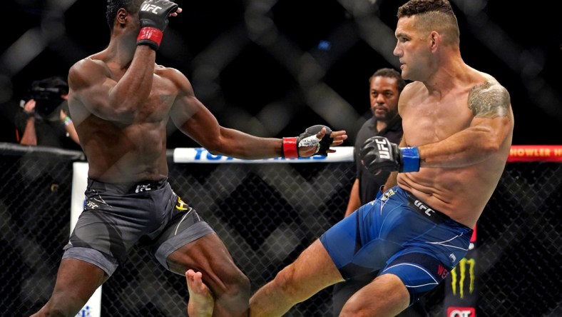 Apr 24, 2021; Jacksonville, Florida, USA; Chris Weidman (Blue Gloves) breaks his leg on his first kick against Uriah Hall (Red Gloves) during UFC 261 at VyStar Veterans Memorial Arena. Mandatory Credit: Jasen Vinlove-USA TODAY Sports