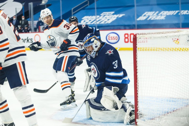 Apr 28, 2021; Winnipeg, Manitoba, CAN;  Winnipeg Jets goalie Connor Hellebuyck (37) makes a save with Edmonton Oilers forward Alex Chiasson (39) looking for a rebound during the first period at Bell MTS Place. Mandatory Credit: Terrence Lee-USA TODAY Sports