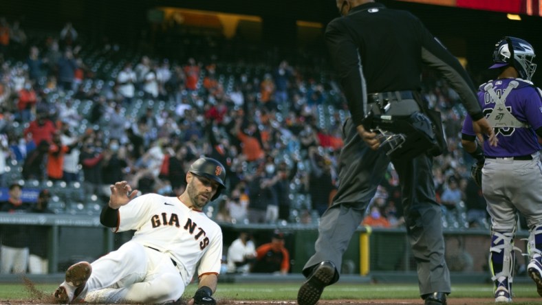 Apr 28, 2021; San Francisco, California, USA; San Francisco Giants catcher Curt Casali (left) slides safely home as he scores on a two-run RBI single hit by first baseman Brandon Belt (9) against the Colorado Rockies during the second inning as home plate umpire CB Bucknor watches at Oracle Park. Mandatory Credit: D. Ross Cameron-USA TODAY Sports