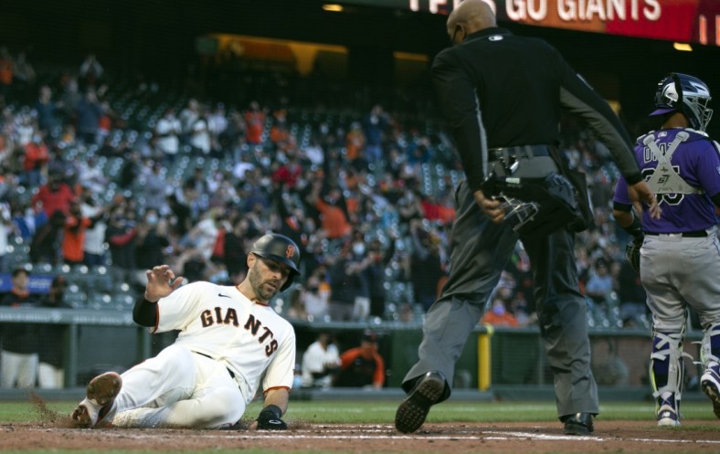 Apr 28, 2021; San Francisco, California, USA; San Francisco Giants catcher Curt Casali (left) slides safely home as he scores on a two-run RBI single hit by first baseman Brandon Belt (9) against the Colorado Rockies during the second inning as home plate umpire CB Bucknor watches at Oracle Park. Mandatory Credit: D. Ross Cameron-USA TODAY Sports