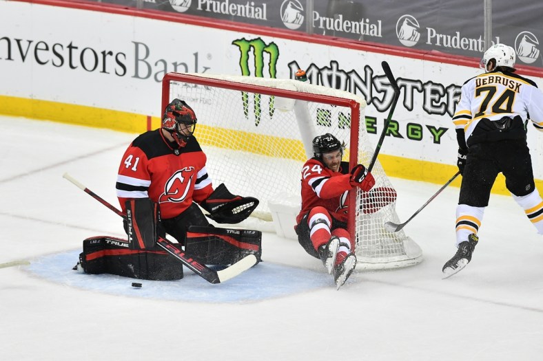 May 3, 2021; Newark, New Jersey, USA; New Jersey Devils defenseman Ty Smith (24) slides into the goal while defending a shot against Boston Bruins left wing Jake DeBrusk (74) during the first period at Prudential Center. Mandatory Credit: Catalina Fragoso-USA TODAY Sports