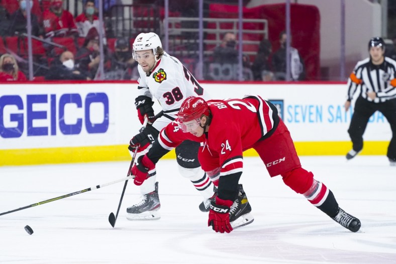 May 4, 2021; Raleigh, North Carolina, USA;  Carolina Hurricanes defenseman Jake Bean (24) and Chicago Blackhawks left wing Brandon Hagel (38 battle for the puck during the first period at PNC Arena. Mandatory Credit: James Guillory-USA TODAY Sports