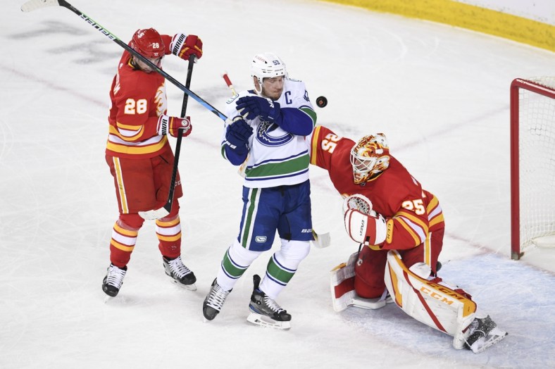 May 13, 2021; Calgary, Alberta, CAN; Vancouver Canucks forward Bo Horvat (53) dodges a shot from near Calgary Flames forward Elias Lindholm (28) and goalie Jacob Markstrom (25) during the first period at Scotiabank Saddledome. Mandatory Credit: Candice Ward-USA TODAY Sports