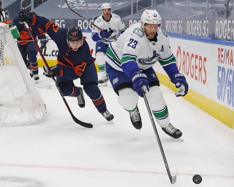 May 15, 2021; Edmonton, Alberta, CAN; Vancouver Canucks defensemen Alex Edler (23) and Edmonton Oilers forward Dominik Kahun (21) chase a loose puck during the third period at Rogers Place. Mandatory Credit: Perry Nelson-USA TODAY Sports
