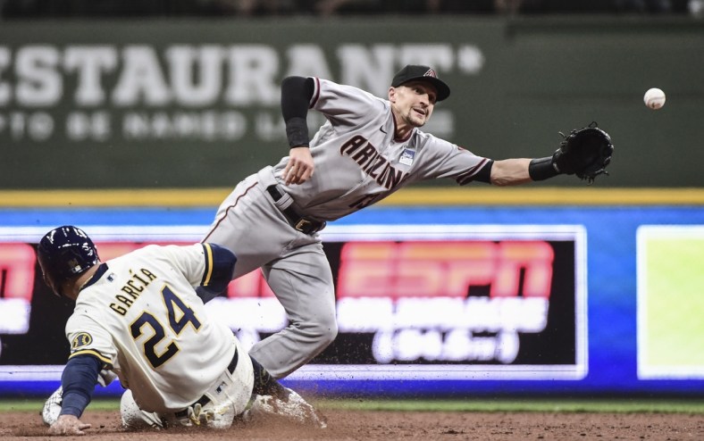Jun 3, 2021; Milwaukee, Wisconsin, USA;  Arizona Diamondbacks shortstop Nick Ahmed (13) reaches for ball on a throwing error by first baseman Christian Walker (not pictured) as Milwaukee Brewers center fielder Avisail Garcia (24) slides advances in the fifth inning at American Family Field. Mandatory Credit: Benny Sieu-USA TODAY Sports