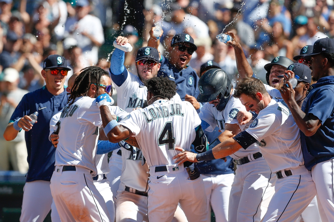 Jun 20, 2021; Seattle, Washington, USA; Seattle Mariners left fielder Shed Long Jr. (4) is mobbed by his teammates at home plate after hitting a walk-off grand slam against the Tampa Bay Rays during the tenth inning at T-Mobile Park. Mandatory Credit: Jennifer Buchanan-USA TODAY Sports