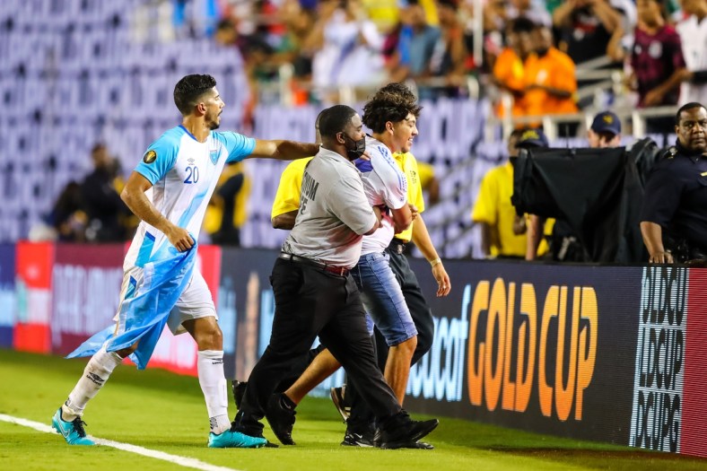 Jul 14, 2021; Dallas, Texas, USA; Guatemala defender Gerardo Gordillo (20) hands a flag back to a fan who ran onto the field during the second half of CONCACAF Gold Cup Soccer group stage play at Cotton Bowl. Mandatory Credit: Ben Ludeman-USA TODAY Sports