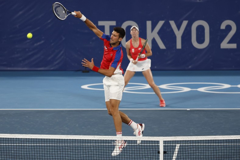 Jul 28, 2021; Tokyo, Japan; Novak Djokovic (L) leaps to hit an overhead in front of partner Nina Stajanovic (R) (both of Serbia) against Marcelo Melo and Luisa Stefari (both of Brazil, not pictured) in a first round mixed doubles match during the Tokyo 2020 Olympic Summer Games at Ariake Tennis Park. Mandatory Credit: Geoff Burke-USA TODAY Sports