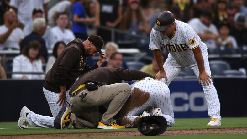 Jul 30, 2021; San Diego, California, USA; San Diego Padres shortstop Fernando Tatis Jr. (second from right) is looked at by a trainer after an injury during the first inning against the Colorado Rockies as Padres manager Jayce Tingler (left) and third base coach Bobby Dickerson (right) look on at Petco Park. Mandatory Credit: Orlando Ramirez-USA TODAY Sports