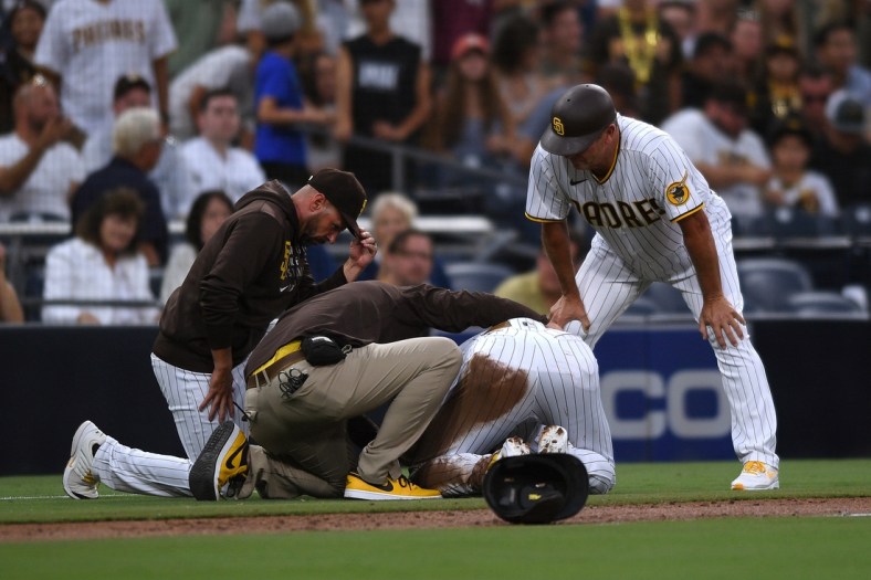 Jul 30, 2021; San Diego, California, USA; San Diego Padres shortstop Fernando Tatis Jr. (second from right) is looked at by a trainer after an injury during the first inning against the Colorado Rockies as Padres manager Jayce Tingler (left) and third base coach Bobby Dickerson (right) look on at Petco Park. Mandatory Credit: Orlando Ramirez-USA TODAY Sports