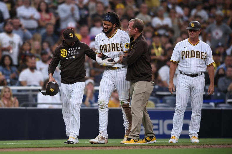 Jul 30, 2021; San Diego, California, USA; San Diego Padres shortstop Fernando Tatis Jr. (second from left) is helped off the field by manager Jayce Tingler (left) and a trainer after an injury during the first inning against the Colorado Rockies at Petco Park. Mandatory Credit: Orlando Ramirez-USA TODAY Sports