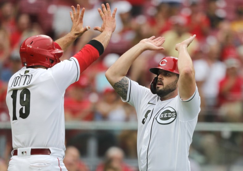 Aug 6, 2021; Cincinnati, Ohio, USA; Cincinnati Reds third baseman Mike Moustakas (right) reacts with first baseman Joey Votto (19) after scoring against the Pittsburgh Pirates during the first inning at Great American Ball Park. Mandatory Credit: David Kohl-USA TODAY Sports