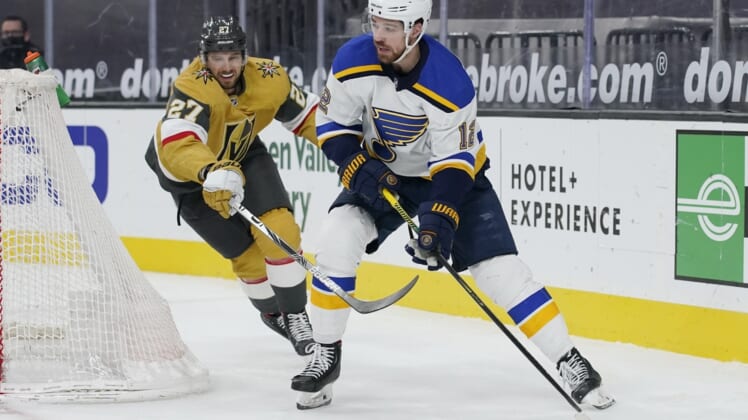 Mar 22, 2021; Las Vegas, Nevada, USA; St. Louis Blues left wing Zach Sanford (12) passes the puck around Vegas Golden Knights defenseman Shea Theodore (27) during the first period at T-Mobile Arena. Mandatory Credit: John Locher /POOL PHOTOS-USA TODAY Sports