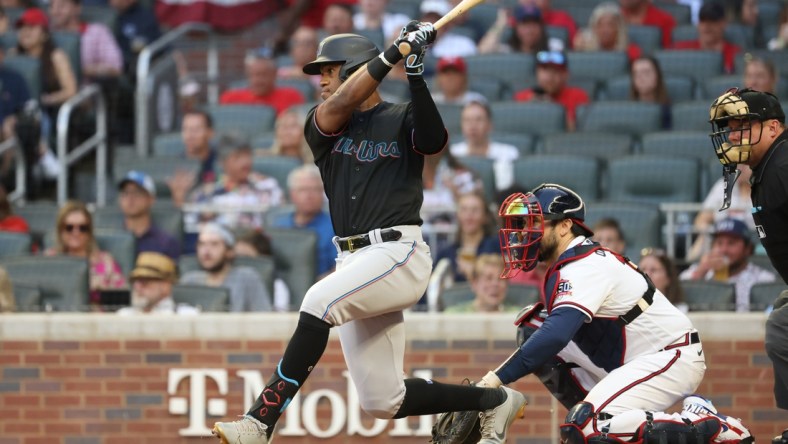 Sep 11, 2021; Atlanta, Georgia, USA; Miami Marlins outfielder Bryan De La Cruz (77) hits an RBI single scoring shortstop Miguel Rojas (not pictured) next to Atlanta Braves catcher Travis d'Arnaud (16) during the first inning at Truist Park. Mandatory Credit: Jason Getz-USA TODAY Sports