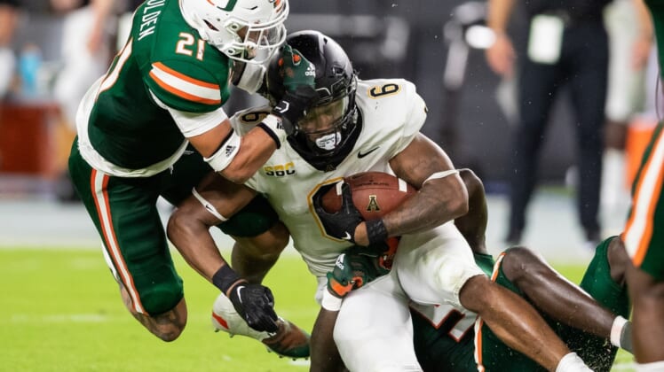 Sep 11, 2021; Miami Gardens, Florida, USA; Appalachian State Mountaineers running back Camerun Peoples (6) is tackled by Miami Hurricanes safety Bubba Bolden (21) and safety Amari Carter (5) during the second quarter at Hard Rock Stadium. Mandatory Credit: Richard Graulich-USA TODAY Sports