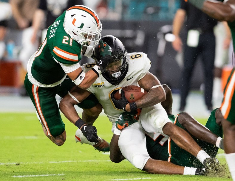 Sep 11, 2021; Miami Gardens, Florida, USA; Appalachian State Mountaineers running back Camerun Peoples (6) is tackled by Miami Hurricanes safety Bubba Bolden (21) and safety Amari Carter (5) during the second quarter at Hard Rock Stadium. Mandatory Credit: Richard Graulich-USA TODAY Sports