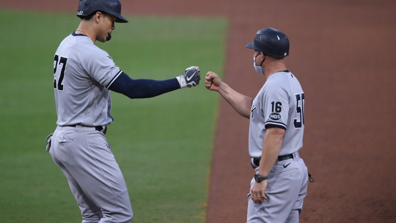 Oct 9, 2020; San Diego, California, USA; New York Yankees designated hitter Giancarlo Stanton (27) fist bumps first base coach Reggie Willits (50) after drawing a walk against the Tampa Bay Rays during the sixth inning of game five of the 2020 ALDS at Petco Park. Mandatory Credit: Orlando Ramirez-USA TODAY Sports