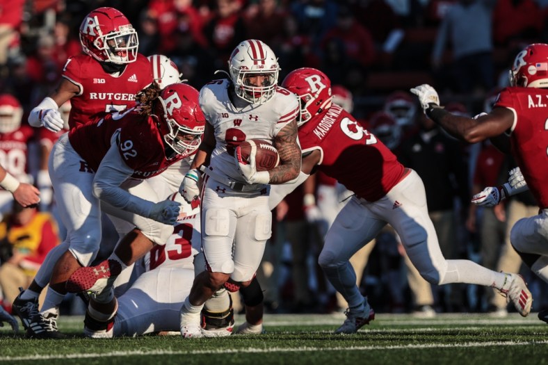 Nov 6, 2021; Piscataway, New Jersey, USA; Wisconsin Badgers running back Chez Mellusi (6) carries the ball as Rutgers Scarlet Knights defensive lineman Mayan Ahanotu (92) and linebacker Tyreek Maddox-Williams (9) pursue  during the first half at SHI Stadium. Mandatory Credit: Vincent Carchietta-USA TODAY Sports