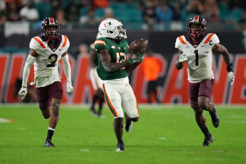 Nov 20, 2021; Miami Gardens, Florida, USA; Miami Hurricanes wide receiver Brashard Smith (12) makes a catch in front of Virginia Tech Hokies defensive back Jermaine Waller (2) and defensive back Chamarri Conner (1) before running for a touchdown in the first half at Hard Rock Stadium. Mandatory Credit: Jasen Vinlove-USA TODAY Sports