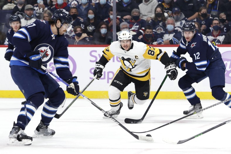 Nov 22, 2021; Winnipeg, Manitoba, CAN; Pittsburgh Penguins center Sidney Crosby (87) and Winnipeg Jets center Jansen Harkins (12) chase down the puck controlled by left wing Adam Lowry (17) in the first period at Canada Life Centre. Mandatory Credit: James Carey Lauder-USA TODAY Sports