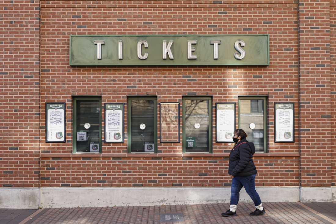 Dec 2, 2021; Chicago, IL, USA; A woman walks by locked Wrigley Field on the first day of Major League Baseball lockout. Mandatory Credit: Kamil Krzaczynski-USA TODAY Sports