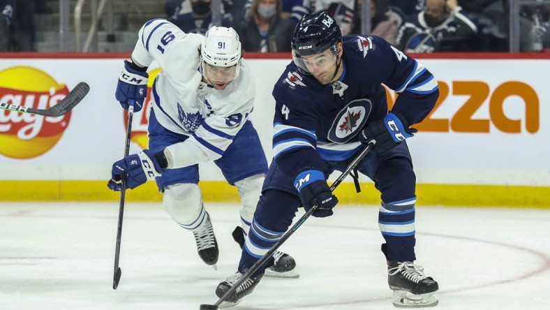 Dec 5, 2021; Winnipeg, Manitoba, CAN; Winnipeg Jets defenseman Neal Pionk (4) skates away from Toronto Maple Leafs forward John Taveres (91) during the first period at Canada Life Centre. Mandatory Credit: Terrence Lee-USA TODAY Sports