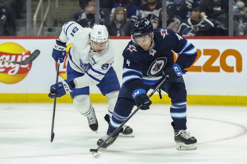 Dec 5, 2021; Winnipeg, Manitoba, CAN; Winnipeg Jets defenseman Neal Pionk (4) skates away from Toronto Maple Leafs forward John Taveres (91) during the first period at Canada Life Centre. Mandatory Credit: Terrence Lee-USA TODAY Sports
