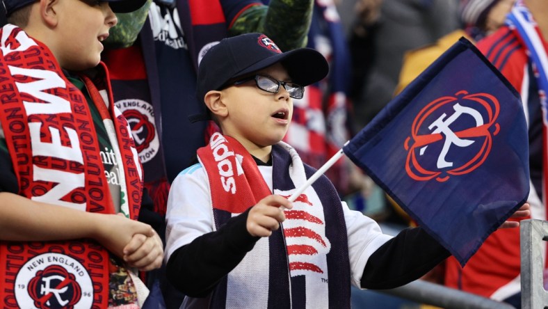 Nov 7, 2021; Foxborough, Massachusetts, USA; A young New England Revolution fan waves a flag with the team   s new logo for the 2022-23 season during the first half of the game between the New England Revolution and the Inter Miami at Gillette Stadium. Mandatory Credit: Winslow Townson-USA TODAY Sports